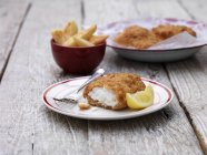 Breaded chunky cod with bowl of french fries on wooden table — Stock Photo