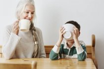 Boy drinking milk from bowl with grandmother — Stock Photo