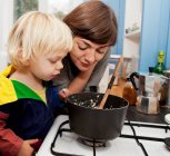 Madre e hijo a la espera de gachas para cocinar en la cocina - foto de stock