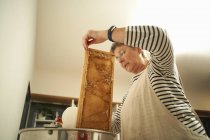 Senior apiculteur femelle gratter nid d'abeille dans une casserole de cuisine — Photo de stock