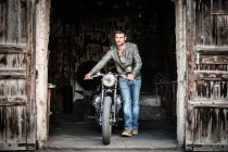 Молодой человек выталкивает мотоцикл из двери сарая — стоковое фото