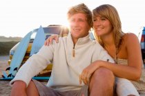Пара сидящих на пляже улыбающихся с фургоном — стоковое фото