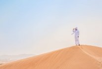 Middle eastern man wearing traditional clothes looking out from desert dune, Dubai, United Arab Emirates — Stock Photo
