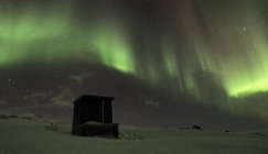 As luzes do norte iluminaram o céu acima da cabine do log na colina snowcapped — Fotografia de Stock