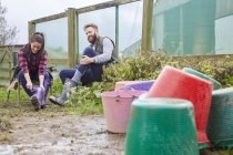 Young couple on farmland putting on rubber boots — Stock Photo