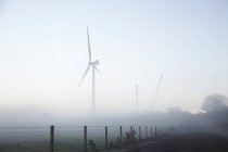 Turbina eólica y grúas en niebla - foto de stock