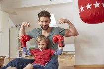 Menino vestindo boxe com o pai, flexionando músculos olhando para a câmera — Fotografia de Stock