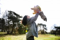 Mature woman holding up and playing with baby son in park — Stock Photo