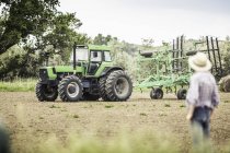 Adolescente ragazzo guardando contadino guida aratro trattore in arato campo — Foto stock