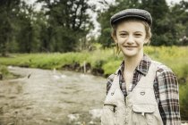Girl wearing flat cap by river smiling — Stock Photo
