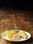 Hühnerkiev mit Käse-Schinken-Füllung auf weißem Teller mit grünen Salatblättern — Stockfoto