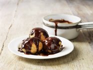 Profiteroles with hot chocolate sauce on white plate — Stock Photo
