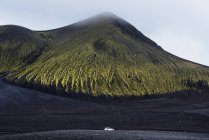 Car parked on black sand under large green hill — Stock Photo