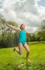 Молода дівчина стрибає над садовим спринклером у полі — стокове фото