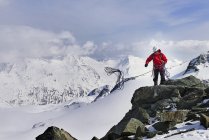 Hombre en la cima de la montaña cubierta de nieve lanzando cuerda de escalada, Saas Fee, Suiza - foto de stock