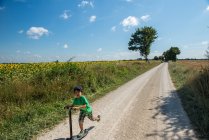 Boy speeding along rural road on scooter, France — Stock Photo