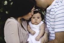 Portrait of baby girl between mother and father in garden — Stock Photo