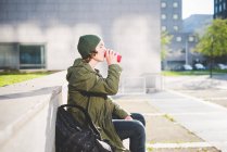 Молодий чоловік, сидячи на міській стіні, п'є з банки — стокове фото