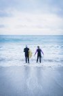 Vue arrière des hommes et des femmes avec planches de surf devant la mer — Photo de stock