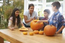 Mother and children carving pumpkin in dining room — Stock Photo