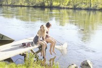 Young women sitting on wooden jetty by water — Stock Photo