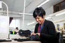 Trabajadora femenina quitando puntos de sutura del paño negro de la máquina de bordado programada de costura rápida en la fábrica de ropa - foto de stock