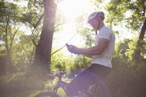 Ciclista usando smartphone en bosque en retroiluminación - foto de stock