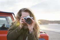Mujer adulta media fotografiando con SLR en estacionamiento costero - foto de stock