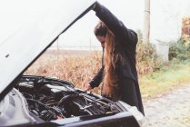 Женщина смотрит на двигатель автомобиля на обочине дороги — стоковое фото