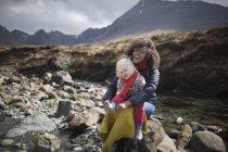 Madre e hijo sentados en las rocas, Piscinas de hadas, Isla de Skye, Hébridas, Escocia - foto de stock