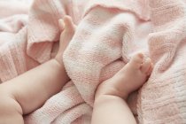 Imagen recortada de las piernas de la niña sobre una manta rosa suave - foto de stock