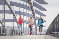Three female runners running on city footbridge — Stock Photo