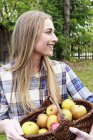 Femme adulte moyenne tenant panier de pommes maison — Photo de stock