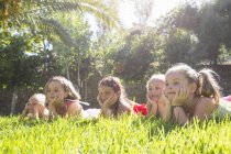 Cinco chicas tumbadas en una fila en el jardín con barbilla en las manos - foto de stock