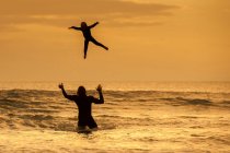 Père jetant son fils dans l'air, dans la mer au coucher du soleil, Lahinch, Clare, Irlande — Photo de stock