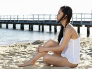 Mujer joven sentada mirando hacia la playa, Port Melbourne, Melbourne, Victoria, Australia - foto de stock