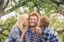 Adolescente chica y joven mujer besando feliz joven hombre en la mejilla - foto de stock