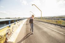 Young woman walking across bridge looking in shoulder bag — Stock Photo