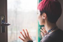 Young woman looking out of window, hands touching window, rear view — Stock Photo