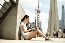 Молодая женщина сидит на мосту глядя на цифровой планшет, Бунд, Шанхай, Китай — стоковое фото