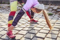 Mid adult female runner doing warm up exercise on cobblestones — Stock Photo