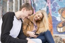 Teenage couple listening to mp3 player against wall with graffiti — Stock Photo