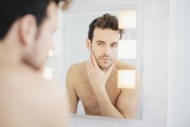 Молодий чоловік перевіряє своє обличчя у дзеркалі ванної кімнати — стокове фото