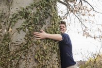 Хлопчик-підліток обіймає широкий стовбур дерева в саду — стокове фото