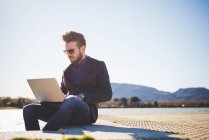 Young man using laptop on lakeside step — Stock Photo