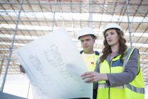 Site manager and architect looking down at blueprint on construction site — Stock Photo