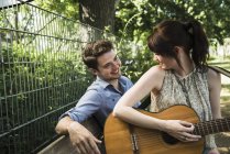 Молода пара грає на акустичній гітарі в парку — стокове фото