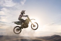 Jeune coureur de motocross masculin silhouetté sautant par-dessus la piste de boue — Photo de stock