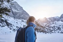 Mujer joven caminando en la nieve y viendo el sol en la cima de la montaña, Austria - foto de stock