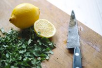Chopped parsley and lemon with knife on wooden board — Stock Photo